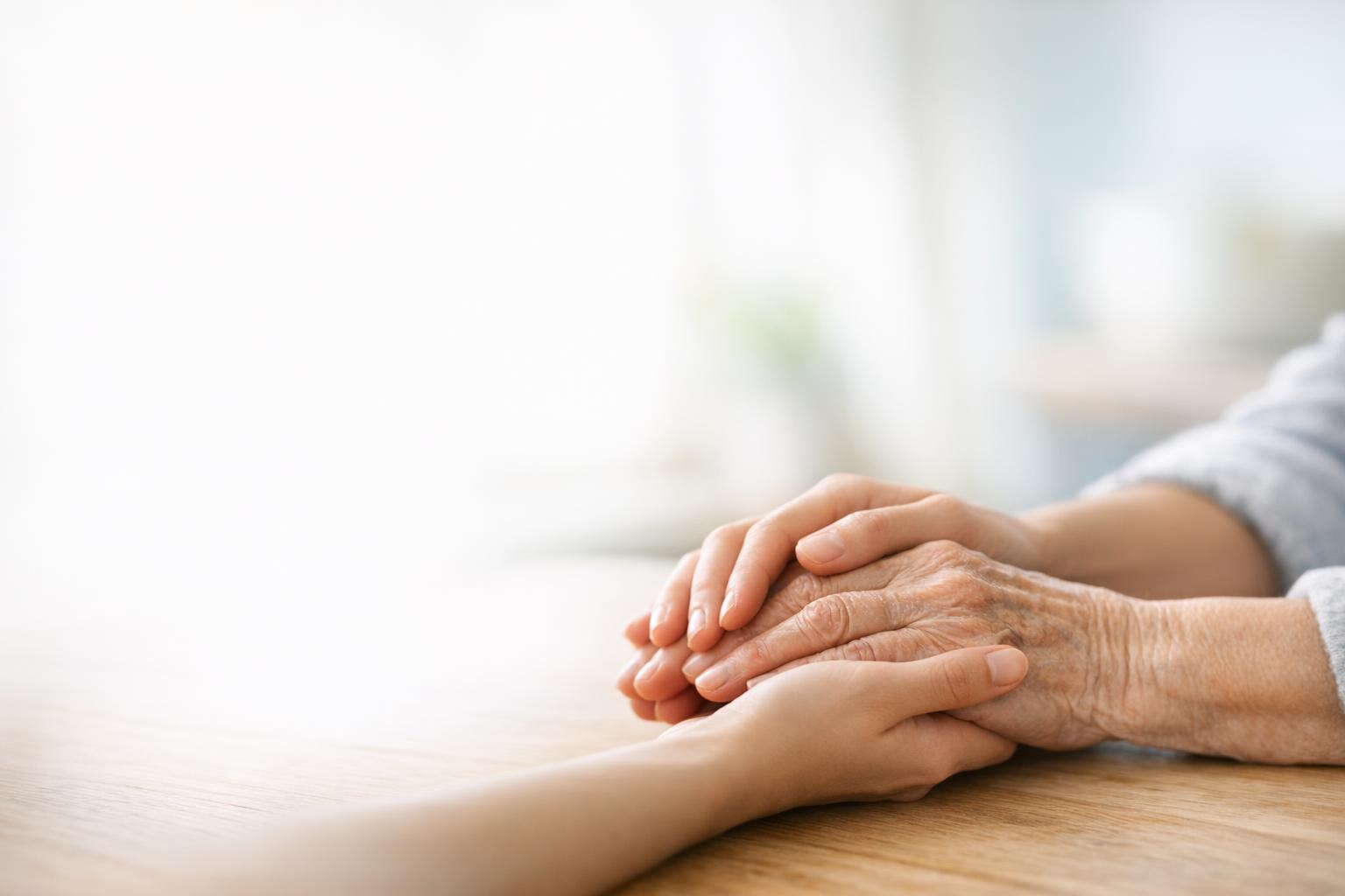 Les mains d'une personne plus jeune tiennent doucement celles d'une personne âgée dans une lumière douce